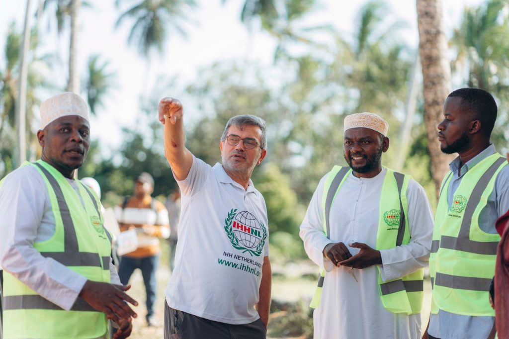Group of adults having a discussion outdoors, wearing high-visibility vests and traditional attire.